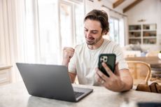 Man checking smartphone and working on laptop at home