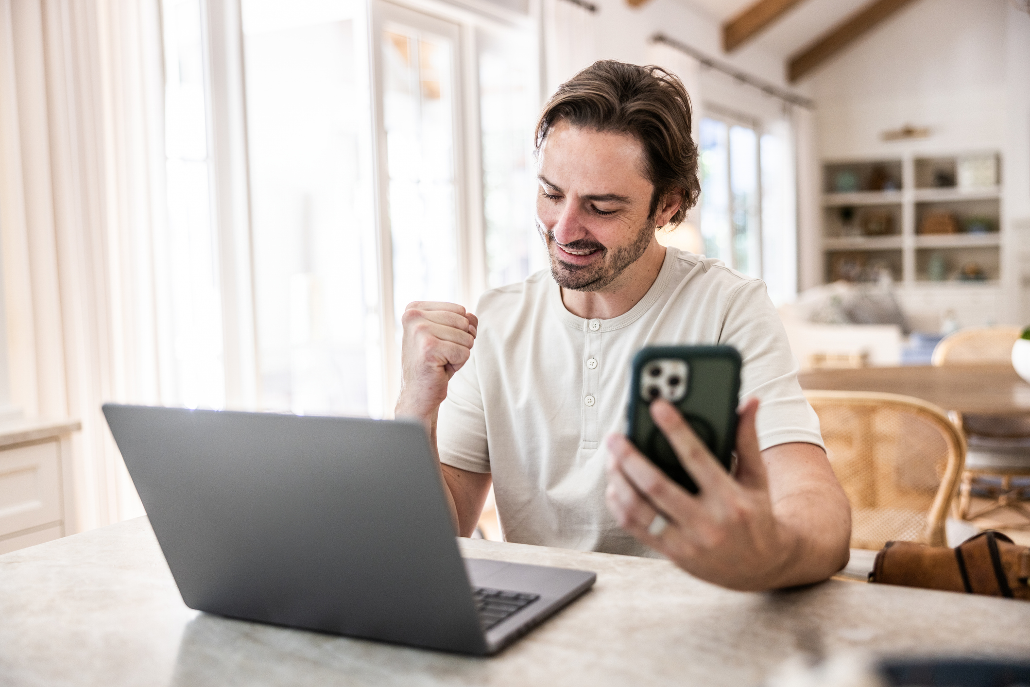 Man checking smartphone and working on laptop at home