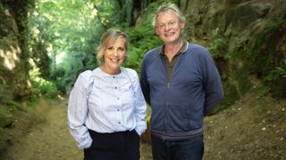 Mel Giedroyc and Martin Clunes stand together in a woodland setting in Mel Giedroyc and Martin Clunes Explore Britain by the Book.