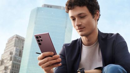 Samsung Galaxy S22 Ultra being used by a young man sitting before a tall building