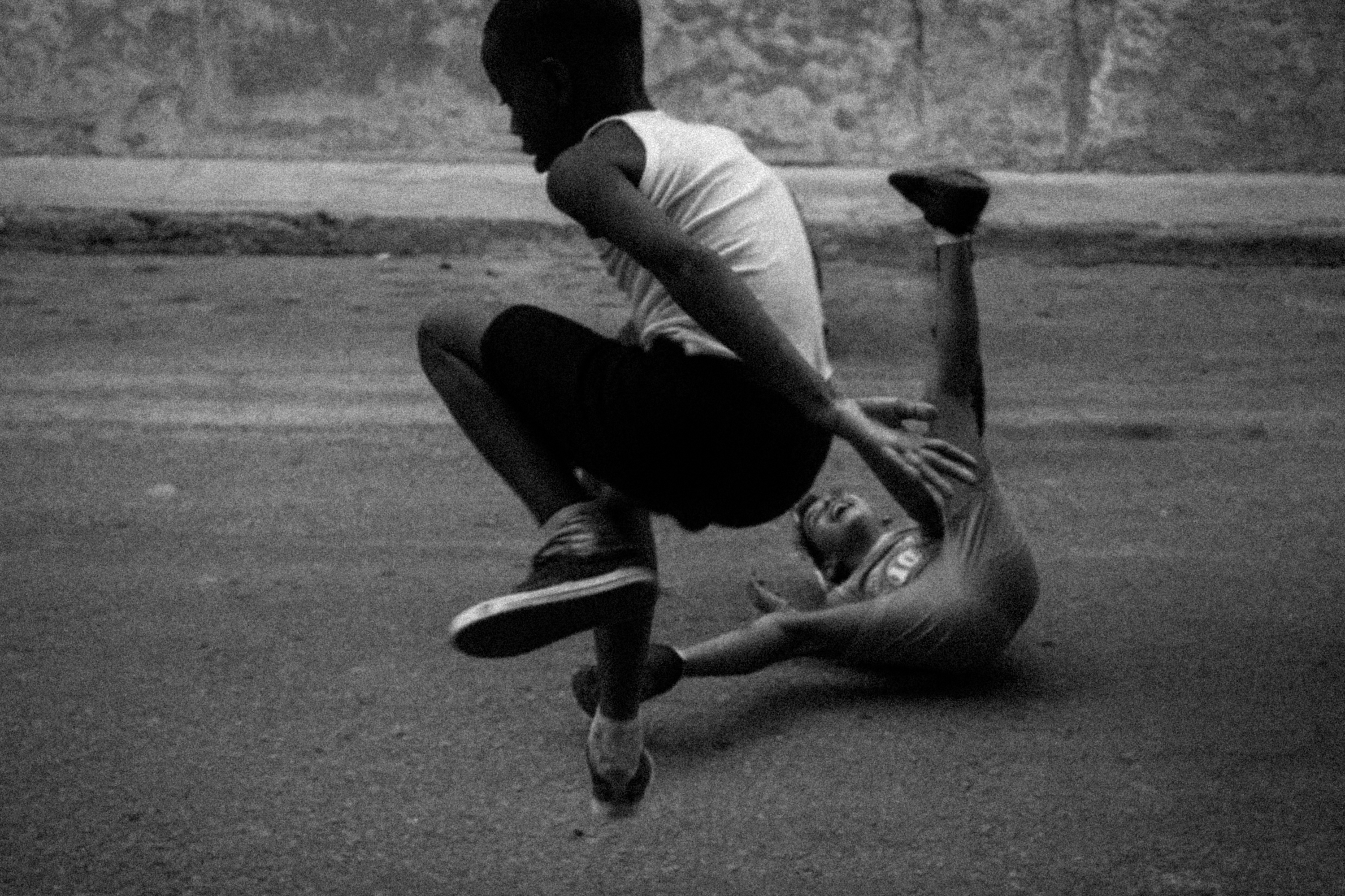 Black and white photograph of two boys captured mid-motion on a Havana street, one flipped upside down in a blurred tumble as the other looks on.