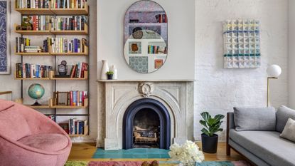 living room with fireplace, white walls, grey sofa, pink armchair and book shelves on left of fireplace