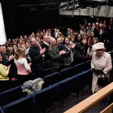 Queen Elizabeth walking into a movie theater and people standing up 
