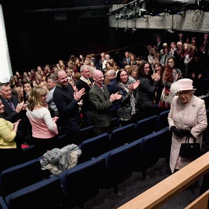 Queen Elizabeth walking into a movie theater and people standing up 