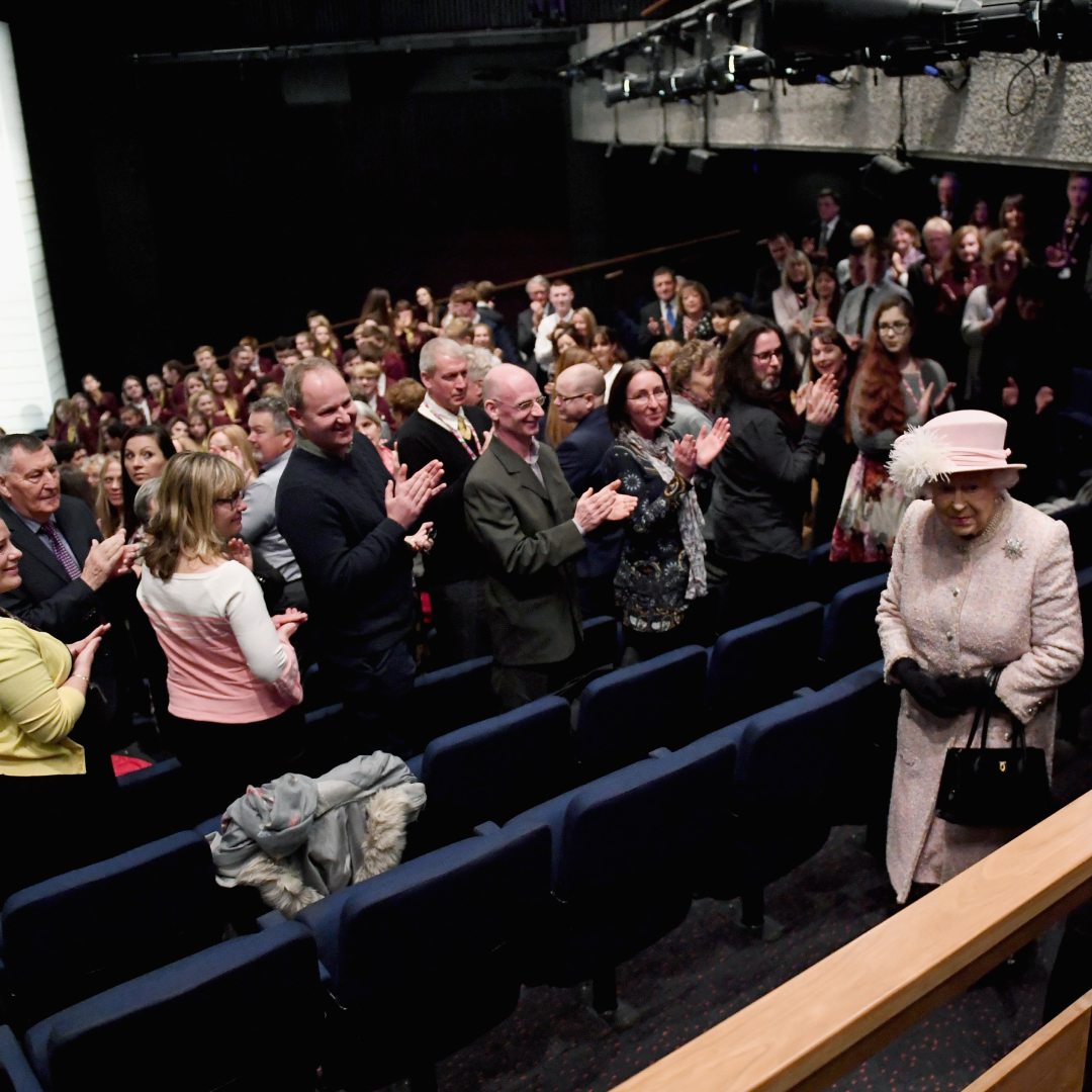Queen Elizabeth walking into a movie theater and people standing up 