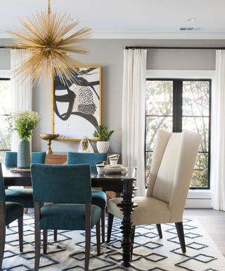 Dining room with light gray painted walls, wooden dining table, blue and cream chairs, patterned rug, gold pendant light