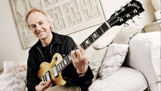 English guitarist Snowy White sits on a sofa playing his guitar