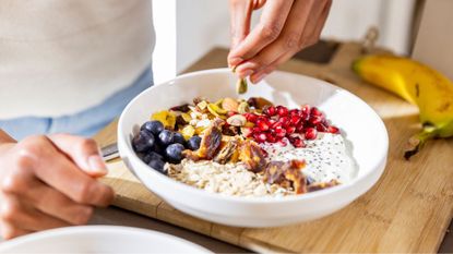 Hands putting fruits and seeds onto a bowl of porridge, a collection of foods that will keep you full