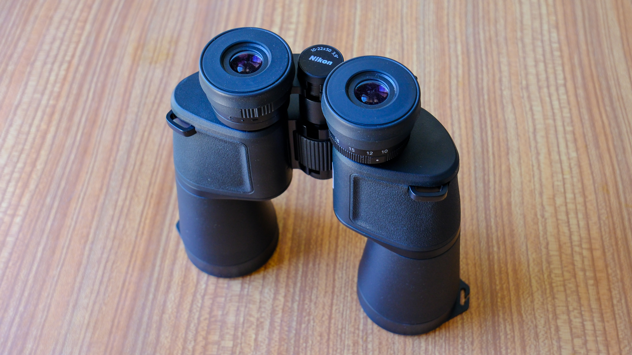The Nikon Action Zoom 10-22x50 binoculars stood upright on a wooden table with the eyecups folded down.