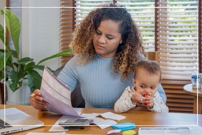 mother holding child looking at bills while sat at a table
