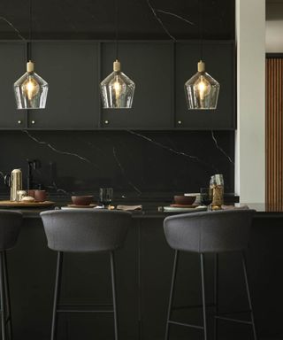 black modern kitchen with island set for breakfast with three glass pendant lights above