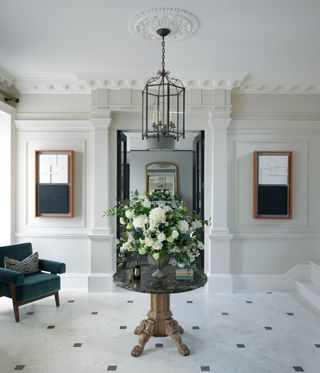 Marble floors, grey walls, glass chandelier with candles and circle table with a bouquet of flowers