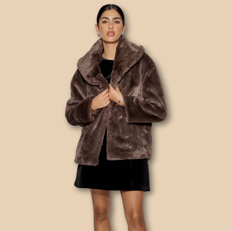 A model wears a brown short faux fur jacket with a black mini skirt