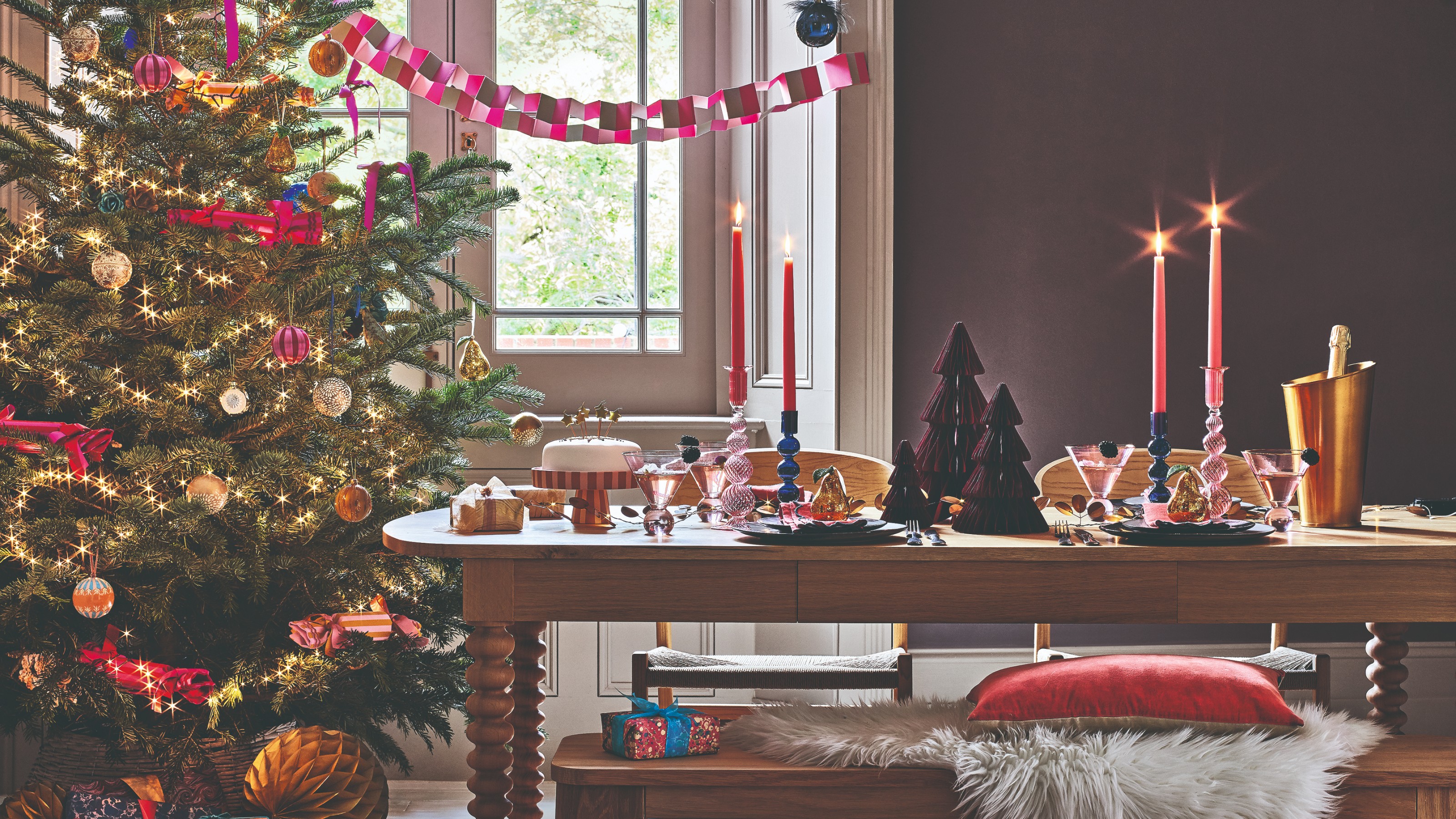 A purple-painted dining room with a decorated Christmas tree in the corner and a set dining table with matching benches