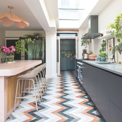 Galley kitchen with dark grey cabinets and colourful chevron floor tiles and a breakfast bar island to the left