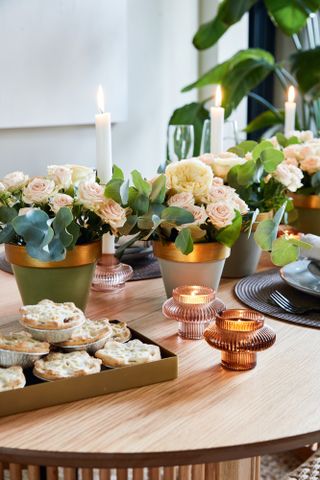 Table with painted flowerpots surrounded by ribbed coloured glass tealight holders and mince pies