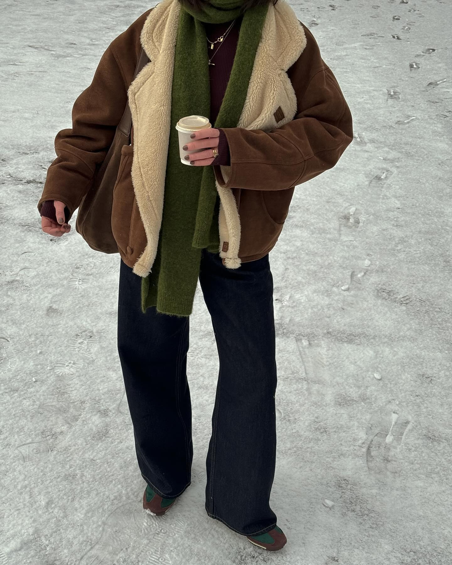 Influencer @francescasaffari stands outside in the snow wearing a sheepskin jacket with flared jeans and brown trainers.