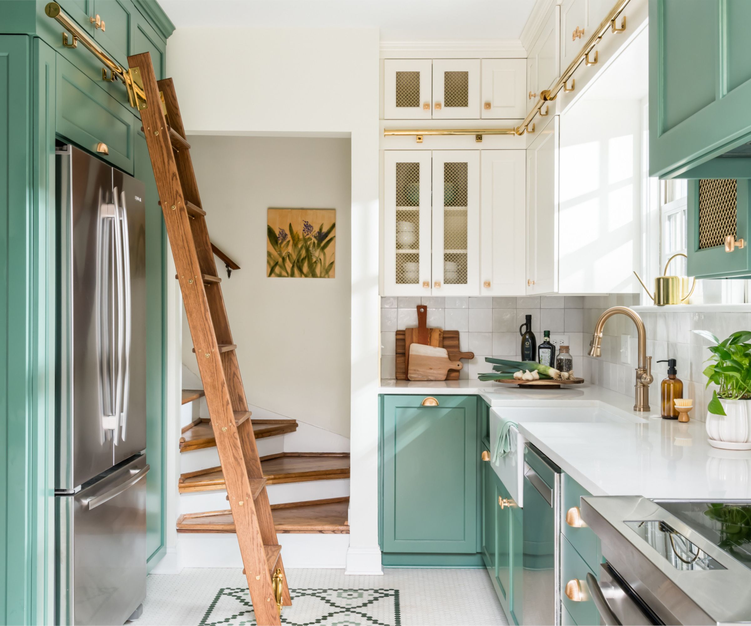 A small kitchen with green cabinets, brass hardware, and a wooden ladder to reach tall storage