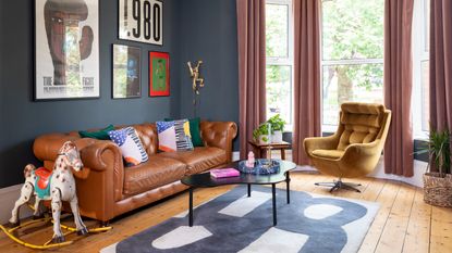 A blue-painted living room with a brown leather Chesterfield sofa and a velvet swivel chair