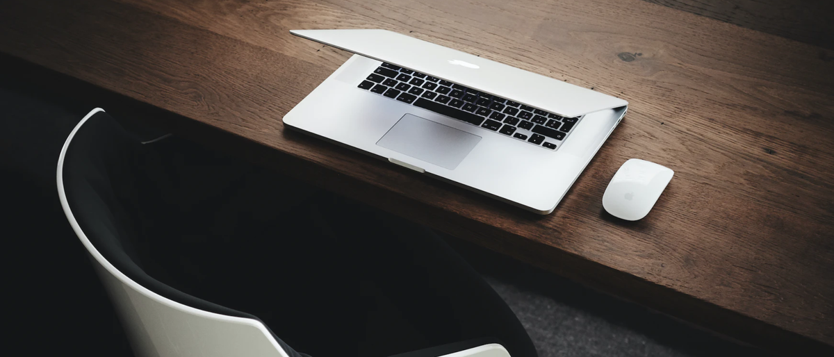 Laptop and mouse on an empty desk beside an empty modernist chair