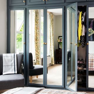 A grey built-in wardrobe with mirror doors, and cupboards up to the ceiling, in a master bedroom
