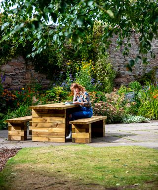 A wooden outdoor table and bench seating in a walled garden