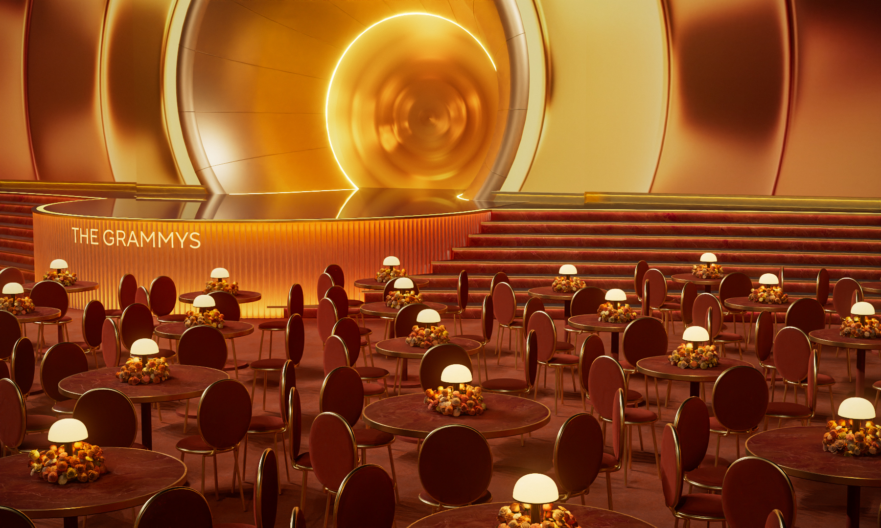 An aerial view of a performance stage with a sculptural, abstract structure of orange, red, and yellow swathes, foregrounded by a series of ceremony round tables with lamps as centerpieces.