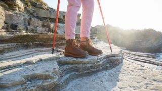 View of woman's walking boots and hiking poles on rocky ledge