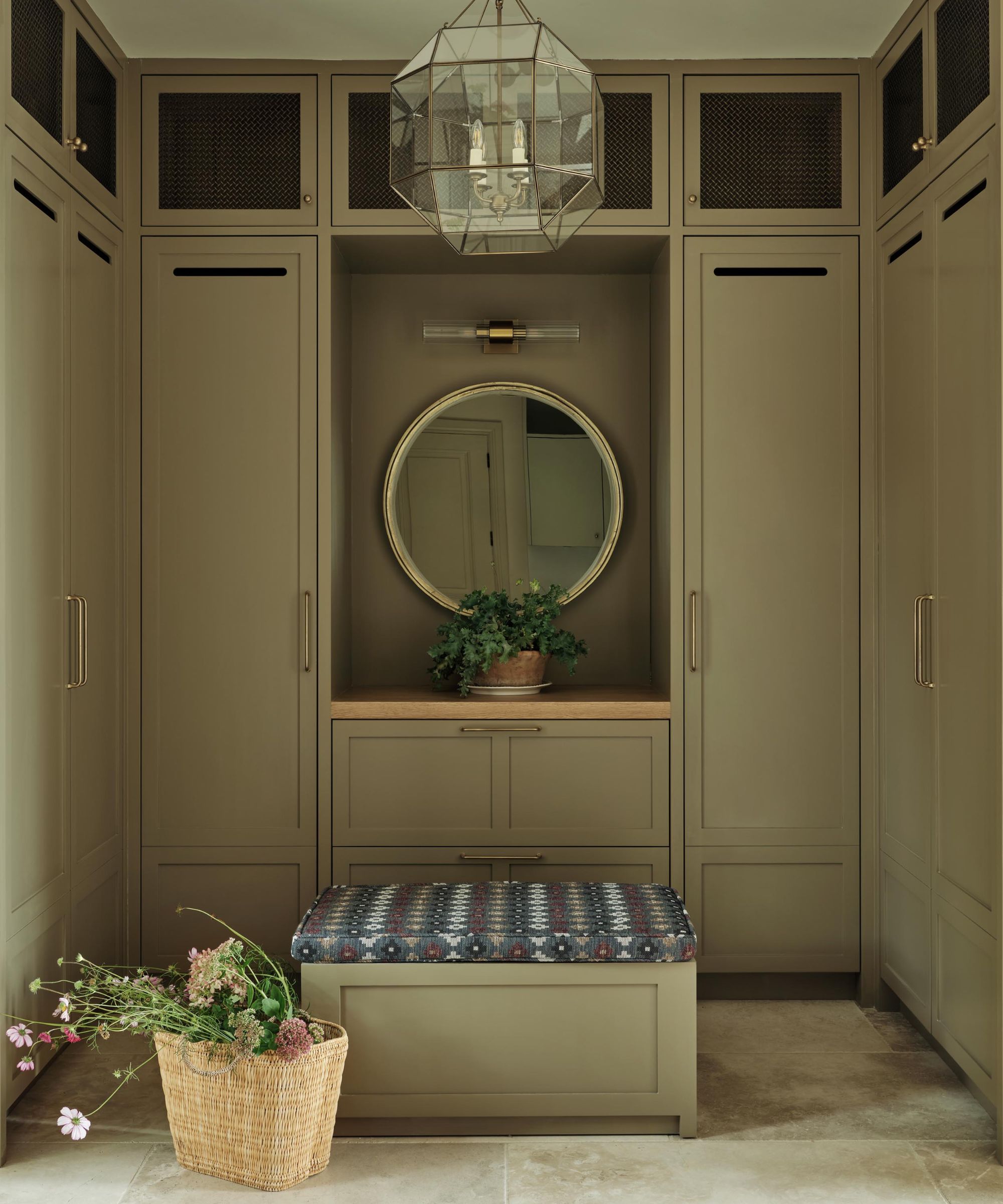 Sage green boot room with built in cabinetry and a square ottoman in the center