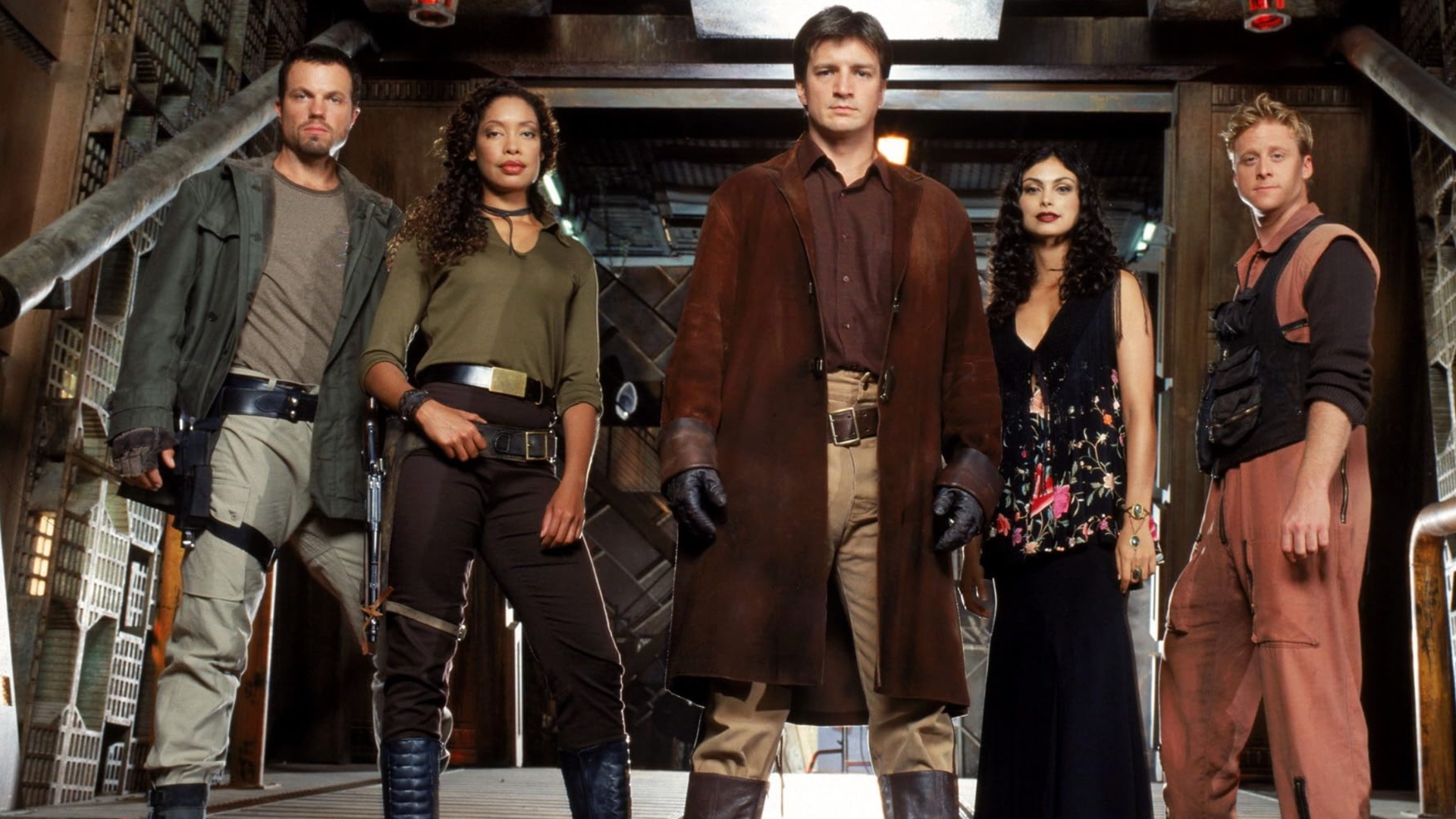 A group of five, three men and two women all look down facing the camera, in an interior hallway