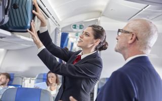 Flight attendant helping businessman place luggage in overhead compartment on airplane