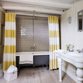 tiled bathroom with yellow shower curtain and roll top bath
