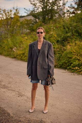 A woman at Copenhagen spring/summer 2025 fashion week wearing a pinstripe blazer, jorts, kitten heels and a bag with bag charms.