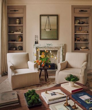 Seating area with two white armchairs next to fireplace and inbuilt bookshelves