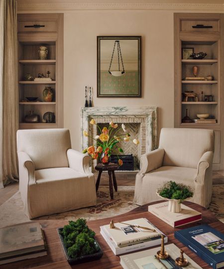 Seating area with two white armchairs next to fireplace and inbuilt bookshelves