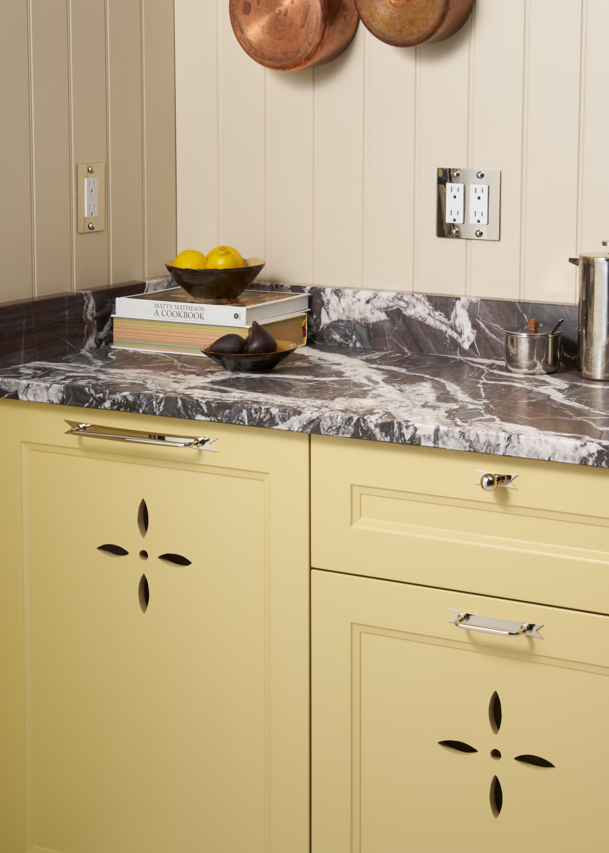 A butter yellow traditional style kitchen with a grey marble worktop and nickel hardware
