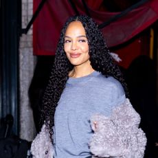 Tessa Thompson wearing a gray sweater, gray fur jacket, black satin skirt, and black boots