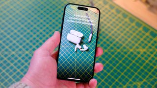 A photo of an iPhone 15 Pro using the Magnifier app to identify a set of AirPods Pro, placed on a green cutting mat