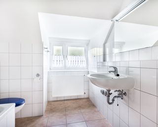 Gleaming tiled bathroom with blue toilet, white sink, and window
