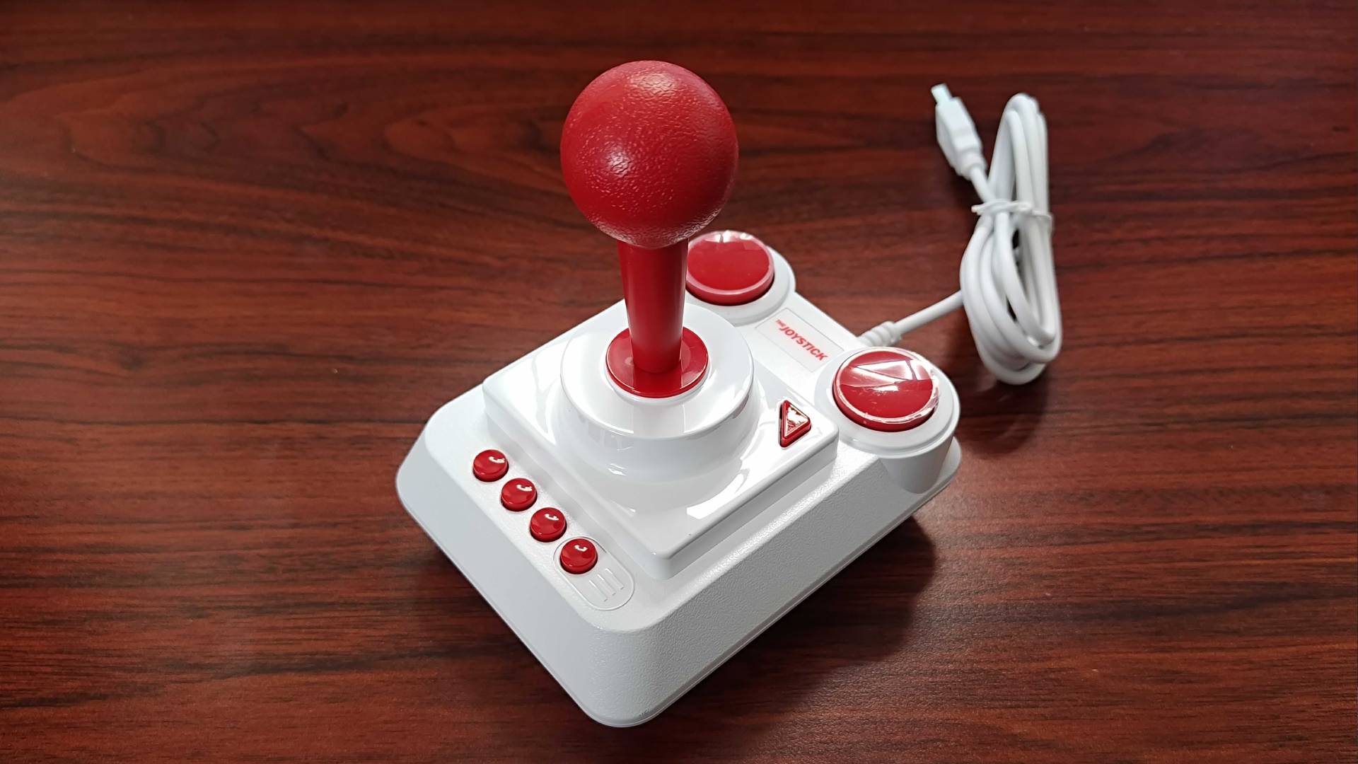The Spectrum joystick in white and red sitting on woodgrain desk.