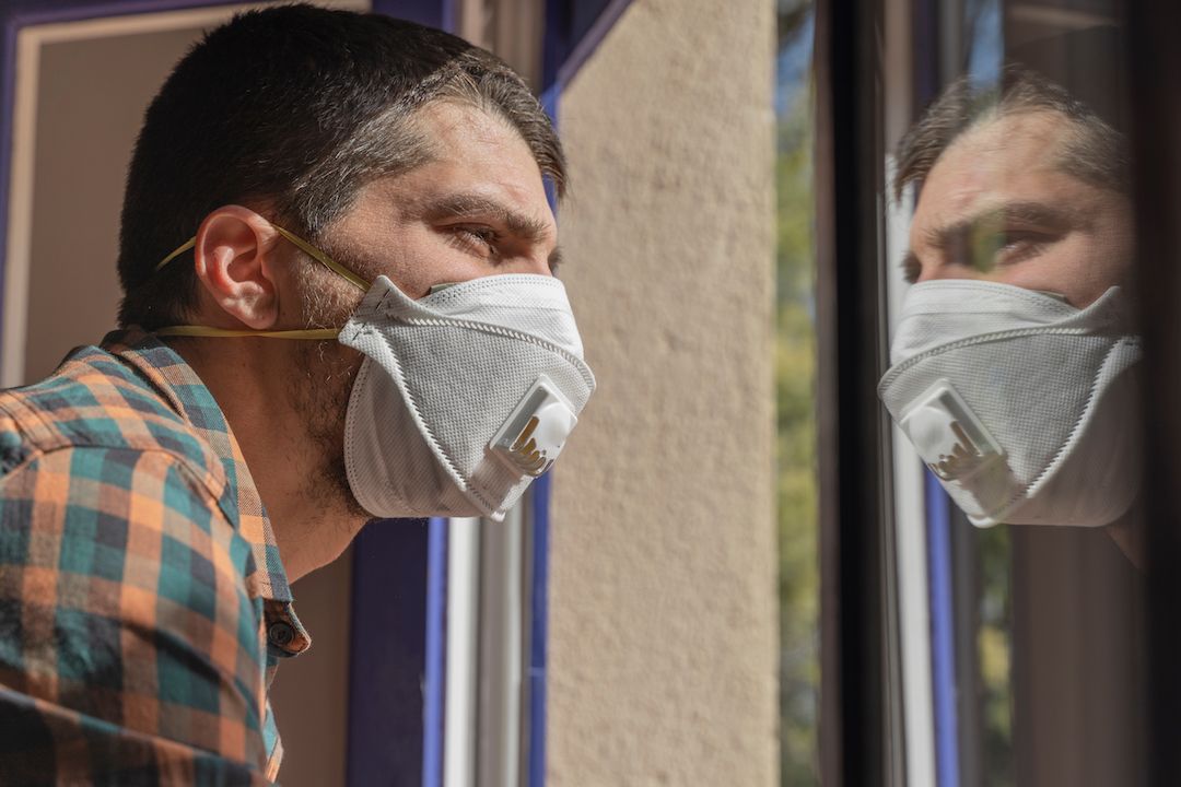 Man in a mask staring out the window.