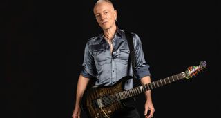 A portrait of Phil Collen against a black background. Collen holds a Jackson s-style