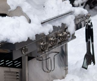 A close up on a gas grill covered in snow