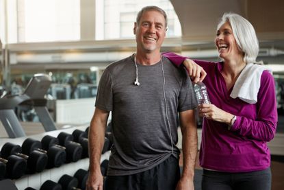Shot of a senior married couple laughing and taking a break from their workout at the gym.