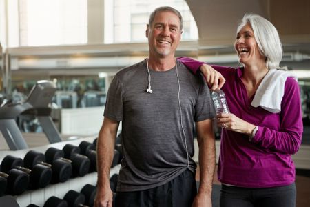 Shot of a senior married couple laughing and taking a break from their workout at the gym.