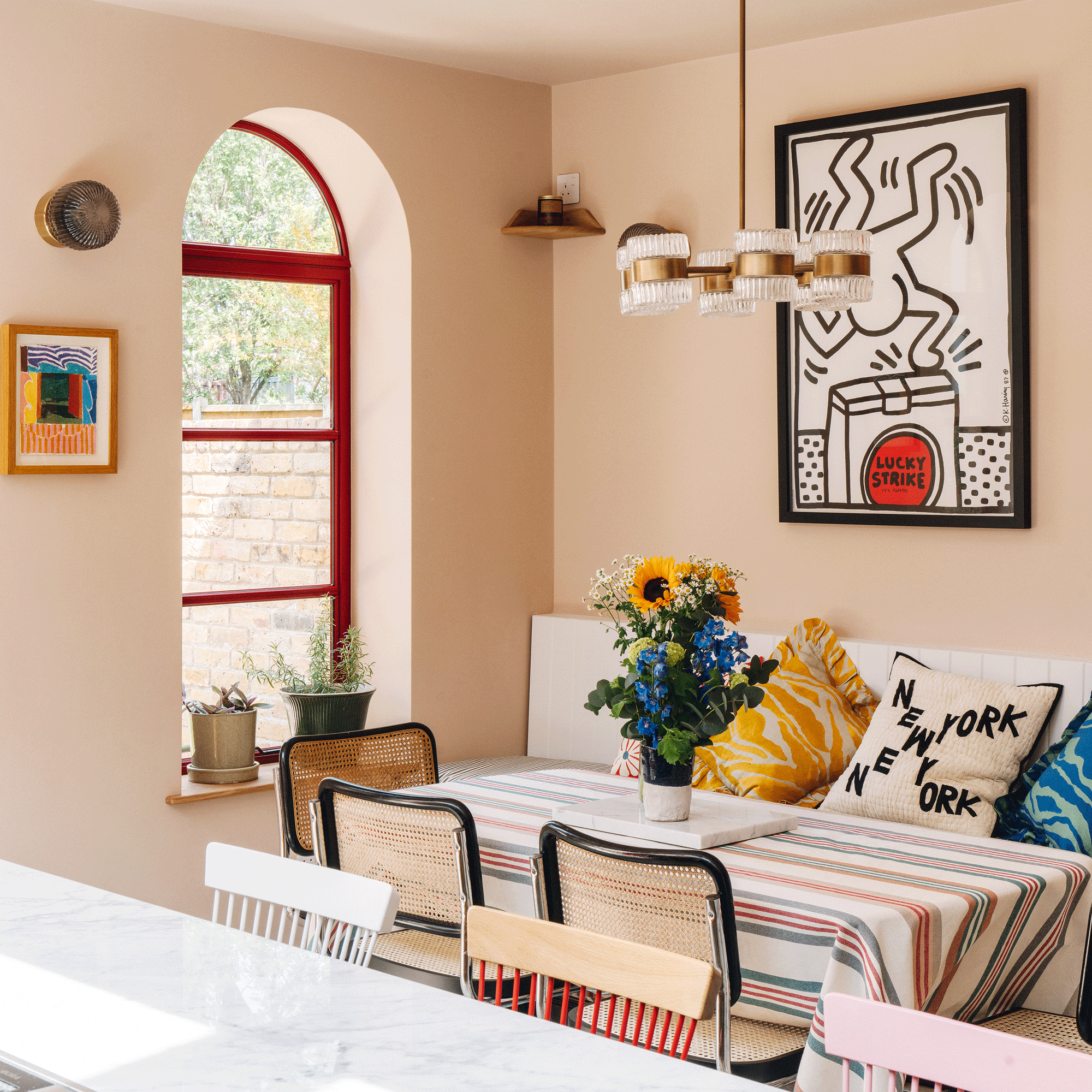 a dining area with an arched window with red framed glazing a dining table with a striped tablecloth and striking wall art