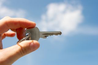 Woman holding door key up against blue sky background