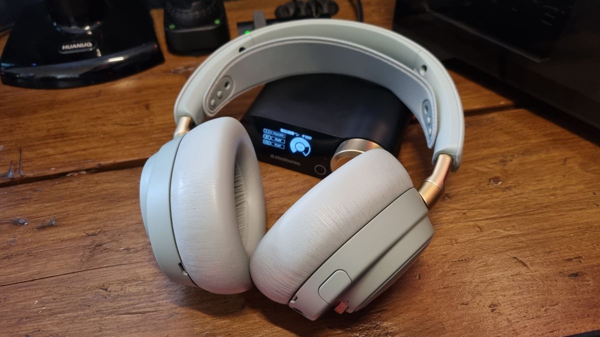 The SteelSeries Arctis Nova Elite gaming headset on a wooden desk, in "sage gold"