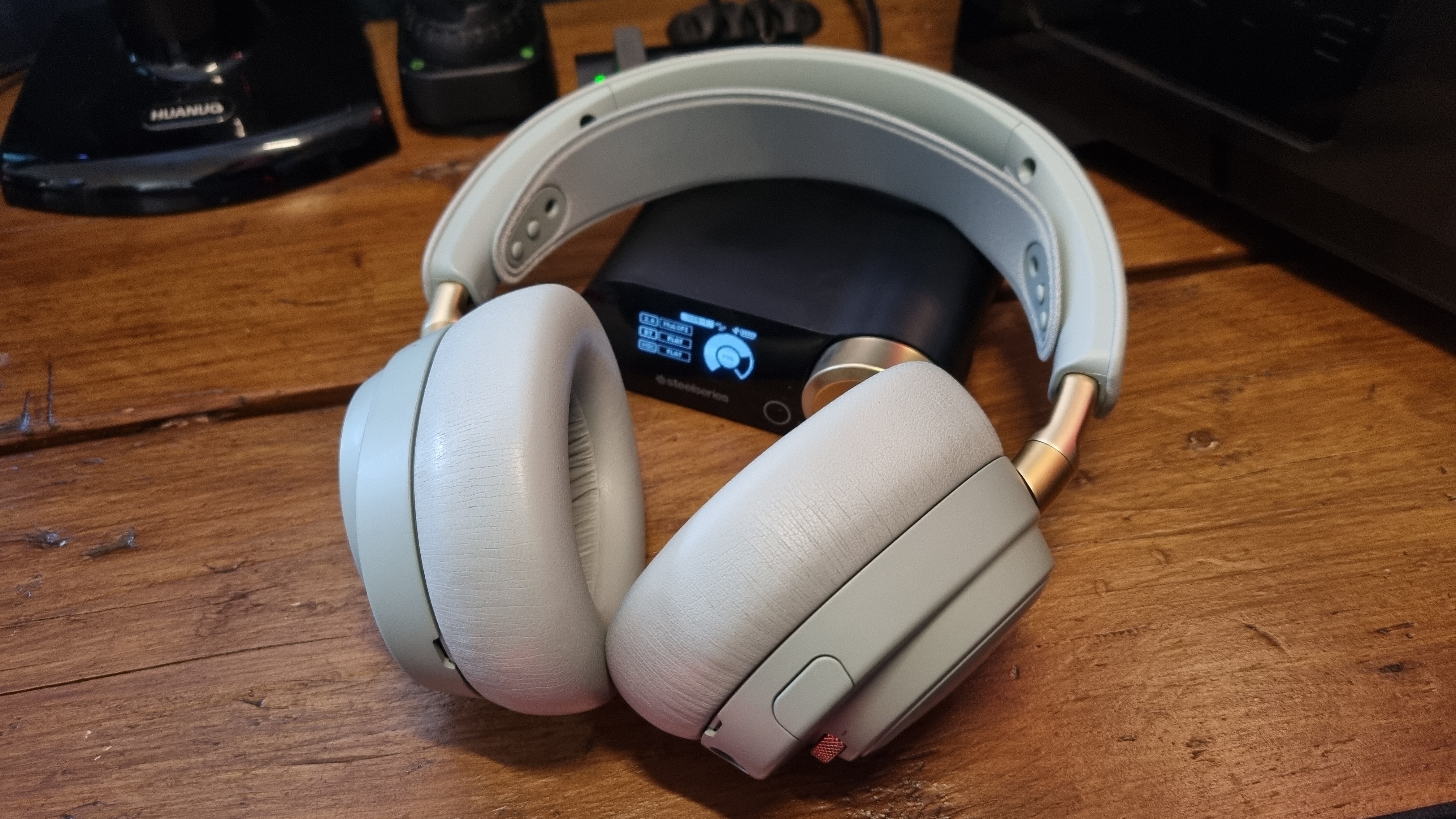 The SteelSeries Arctis Nova Elite gaming headset on a wooden desk, in "sage gold"