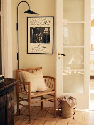 A wooden chair in the corner of a room styled with a moder black wall light and some black and white wall art